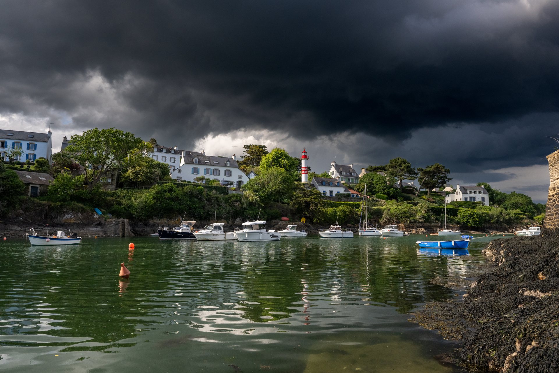 Le port de Doëlan et son phare rouge sous un ciel d'orage