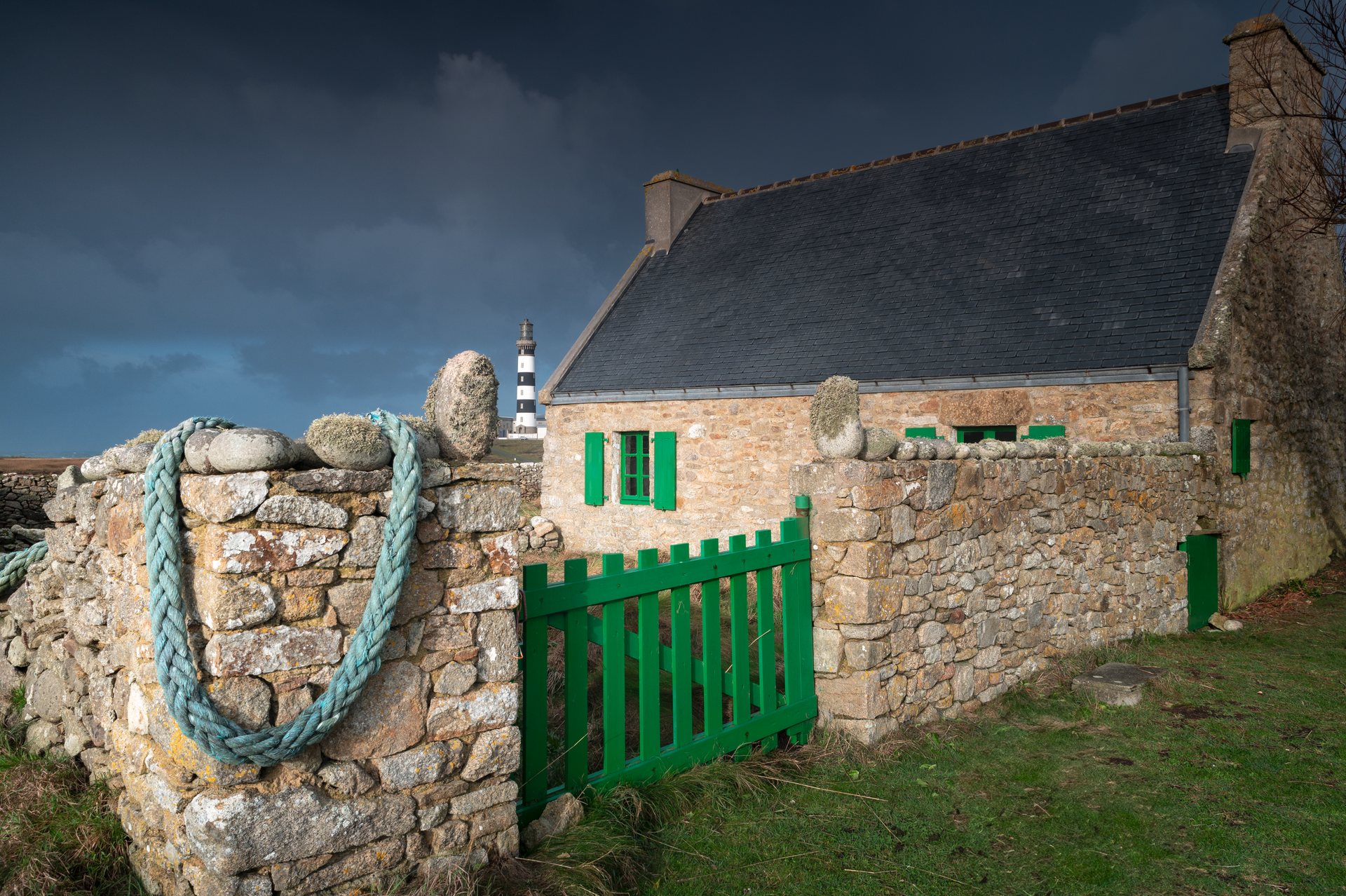 Maison de pierre aux volets verts à Ouessant, le phare du Créac'h au loin